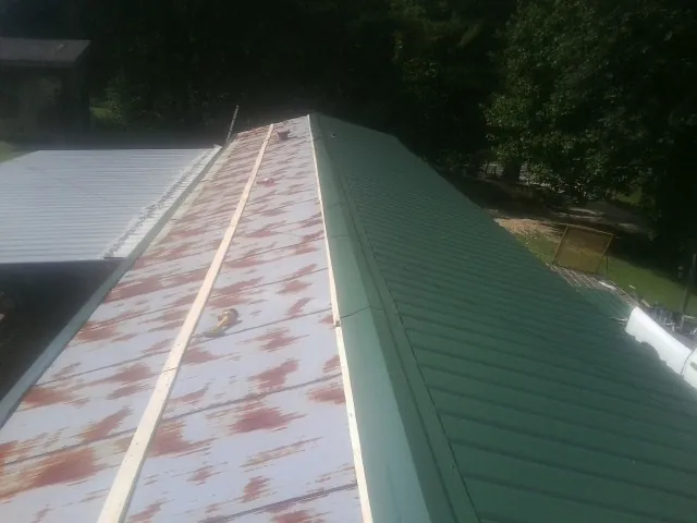 Old rusted panels beside newly installed green metal roofing — Wind Damage Roof Repair by Roofing Brothers in Bushnell