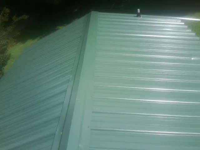New green metal panels meeting at the ridge of a roof — Flat Roof Repair work by our crew in Bushnell